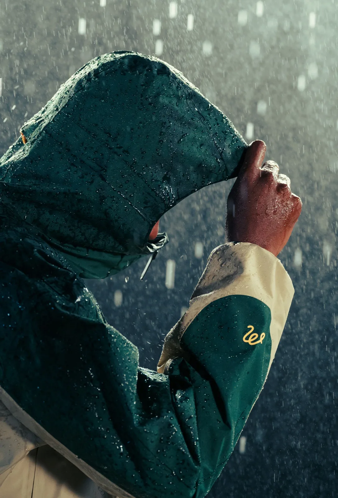 Person pulling up the hood of a dark green GORE-TEX jacket in falling rain